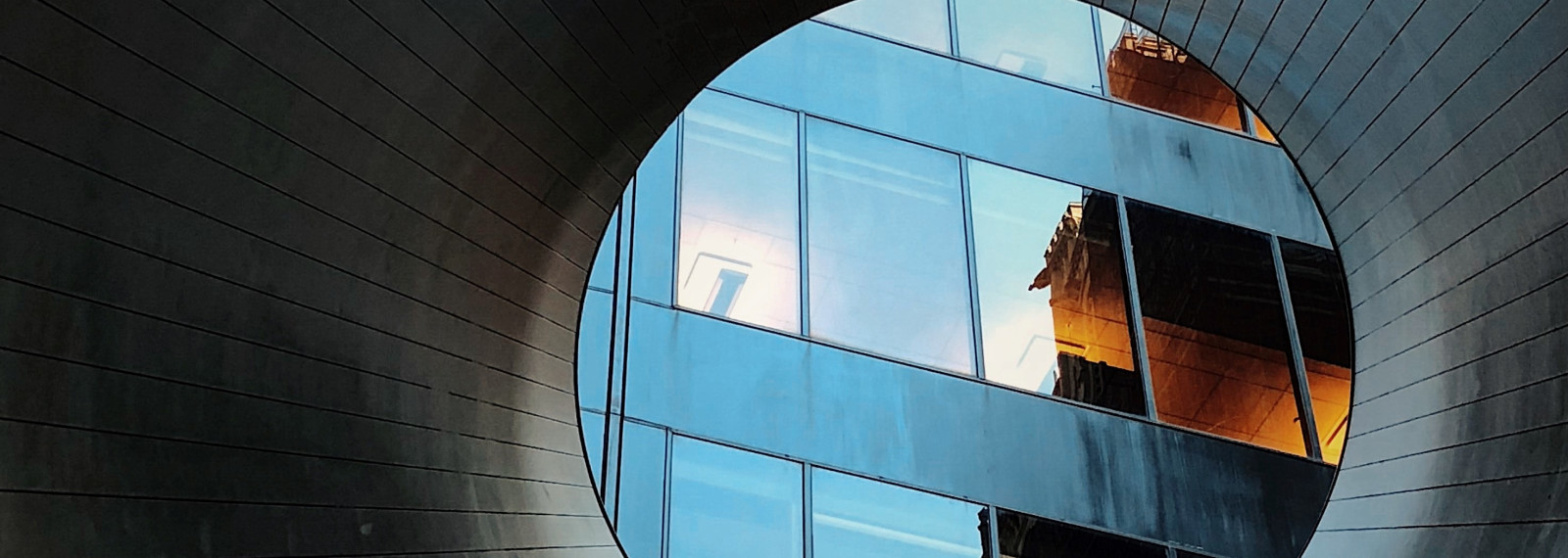 Image looking through a circular tunnel to a corporate building scene