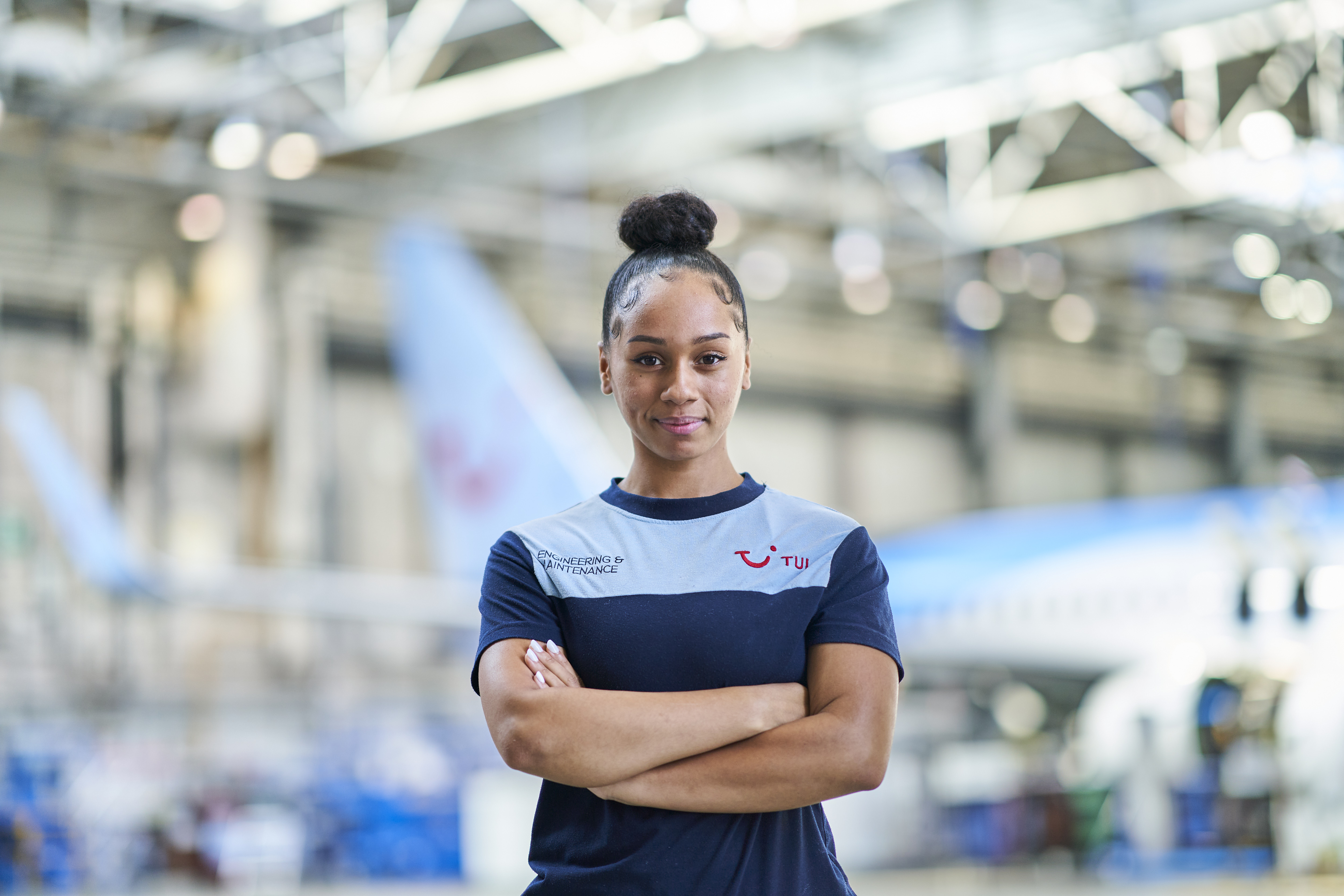 A female aircraft Engineer standing infront of a  TUI aircraft hanger at Luton airport.