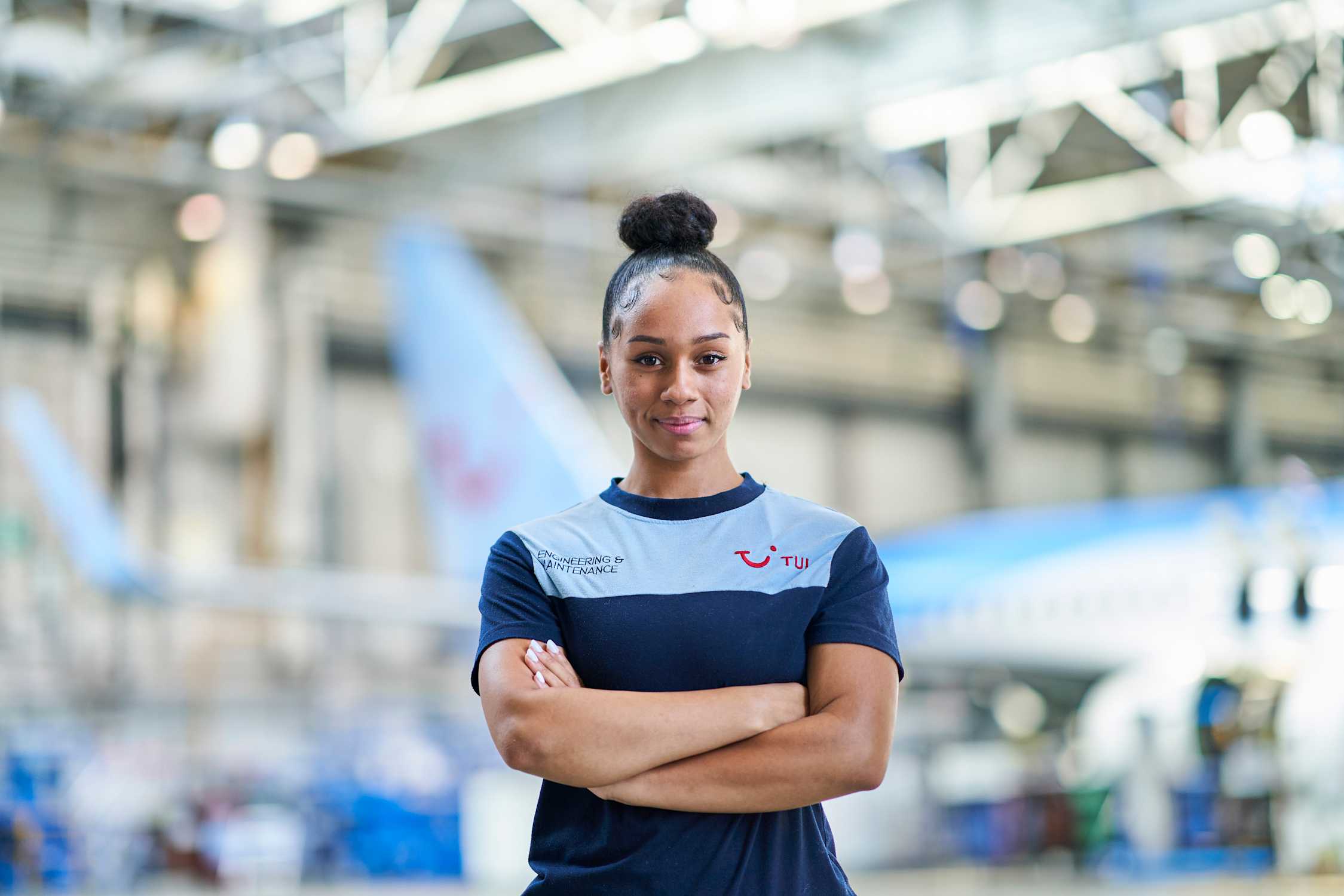 A female aircraft Engineer standing infront of a  TUI aircraft hanger at Luton airport.