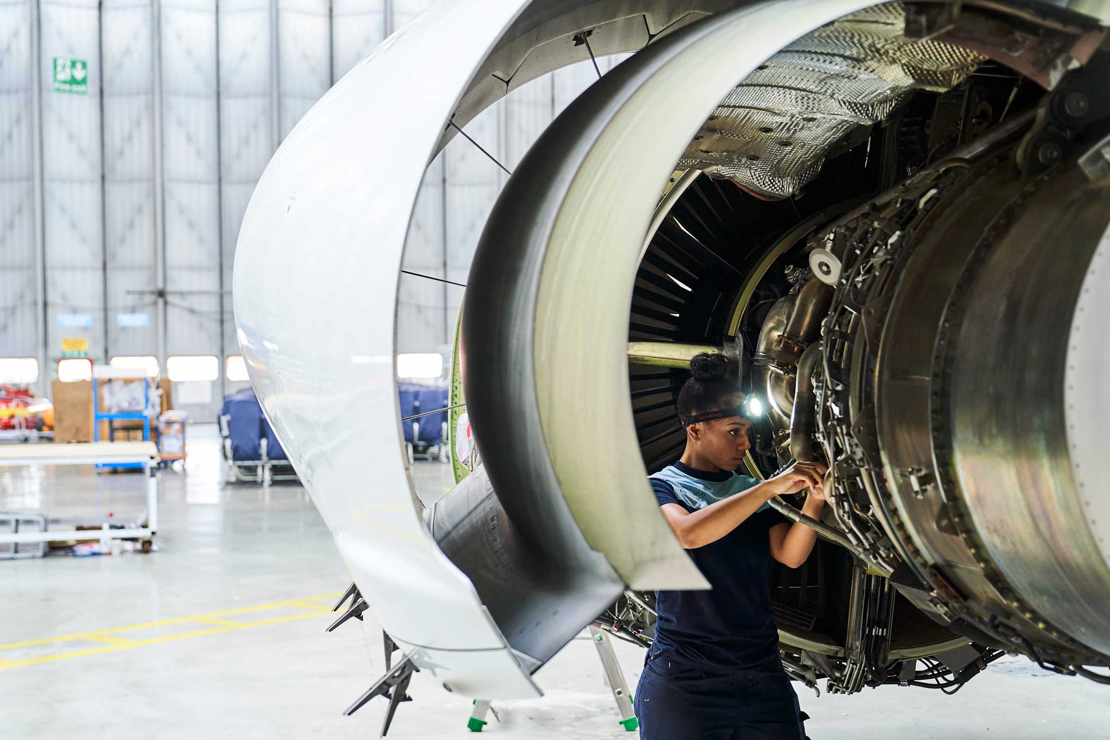 TUI Aircraft Engineer working on a commercial jet turbine inside of an aircraft hanger at Luton airport. She is undergoing servicing and general maintenance tasks.