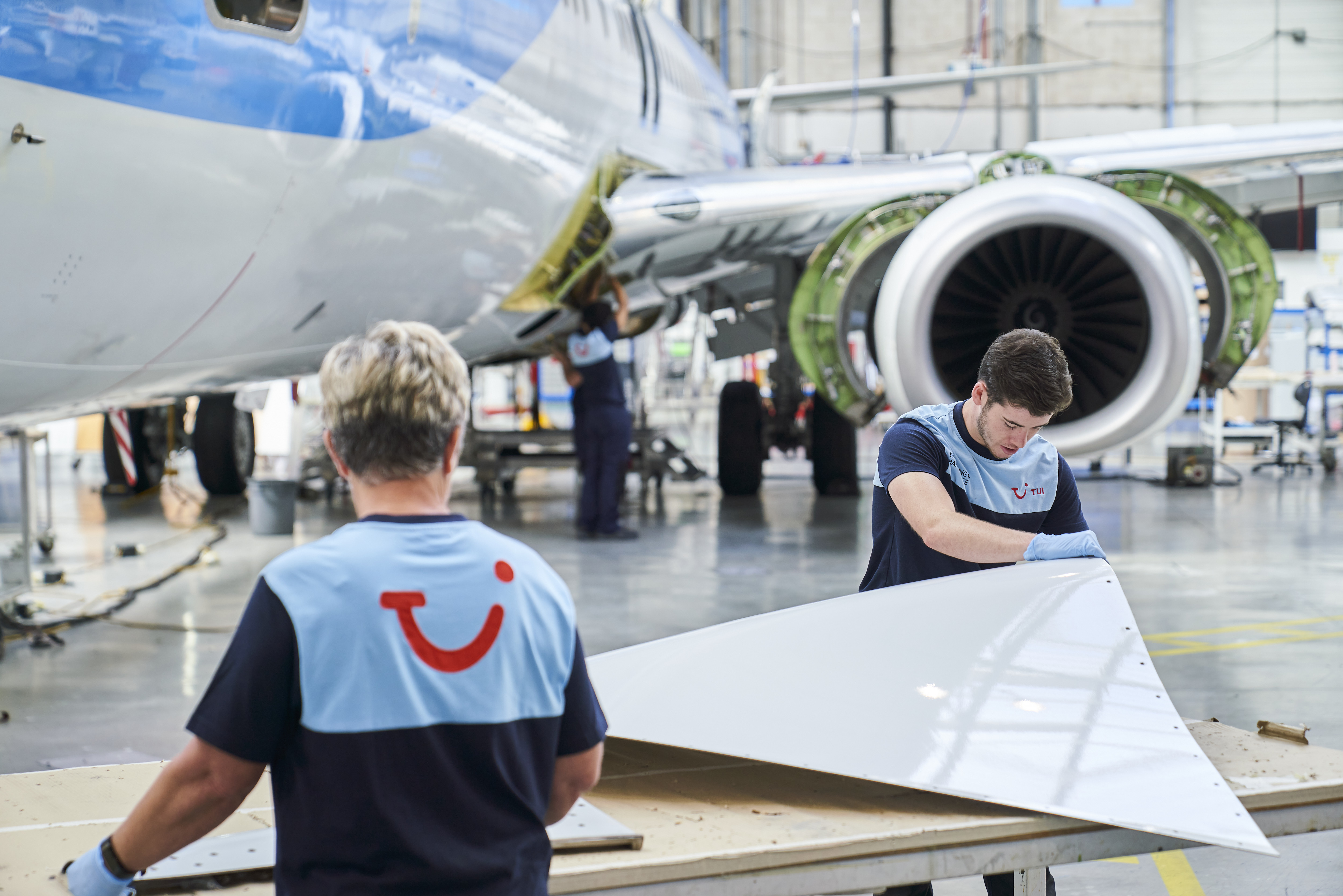 Two TUI aircraft engineers work on a panel of a commercial airplane in Luton airport hanger