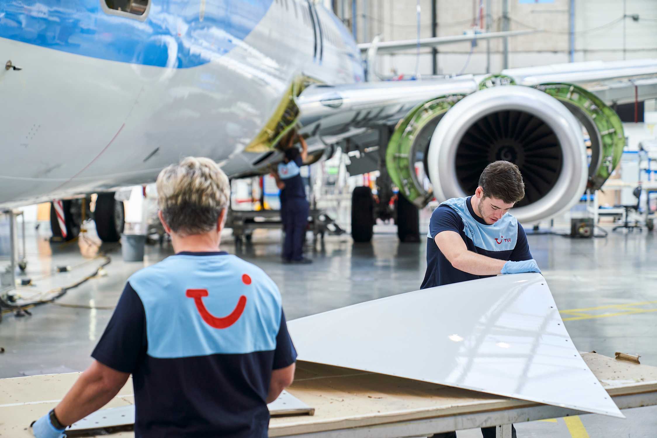 Two TUI aircraft engineers work on a panel of a commercial airplane in Luton airport hanger