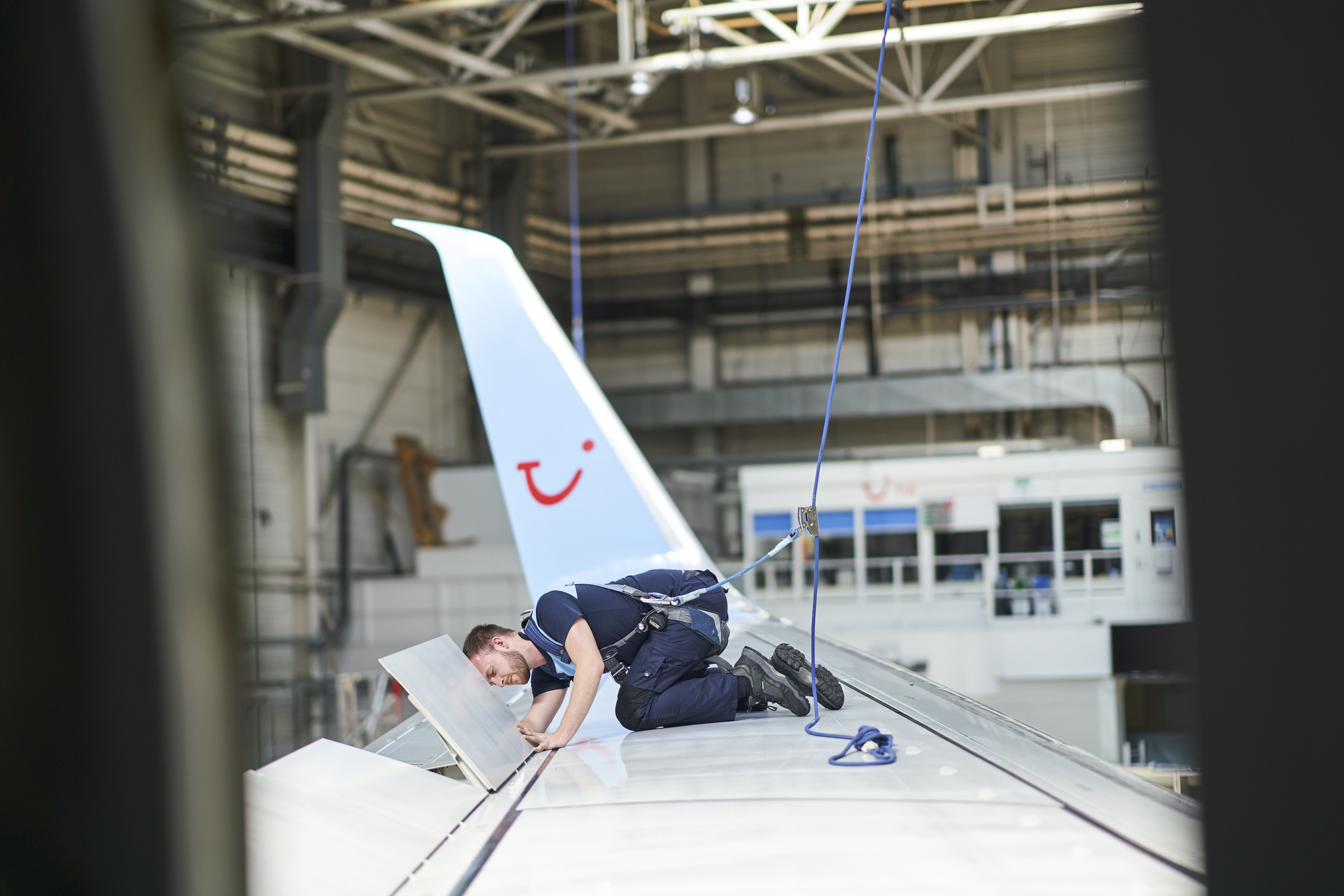 A man works on the flaps of an airplane wing in an aircraft hanger