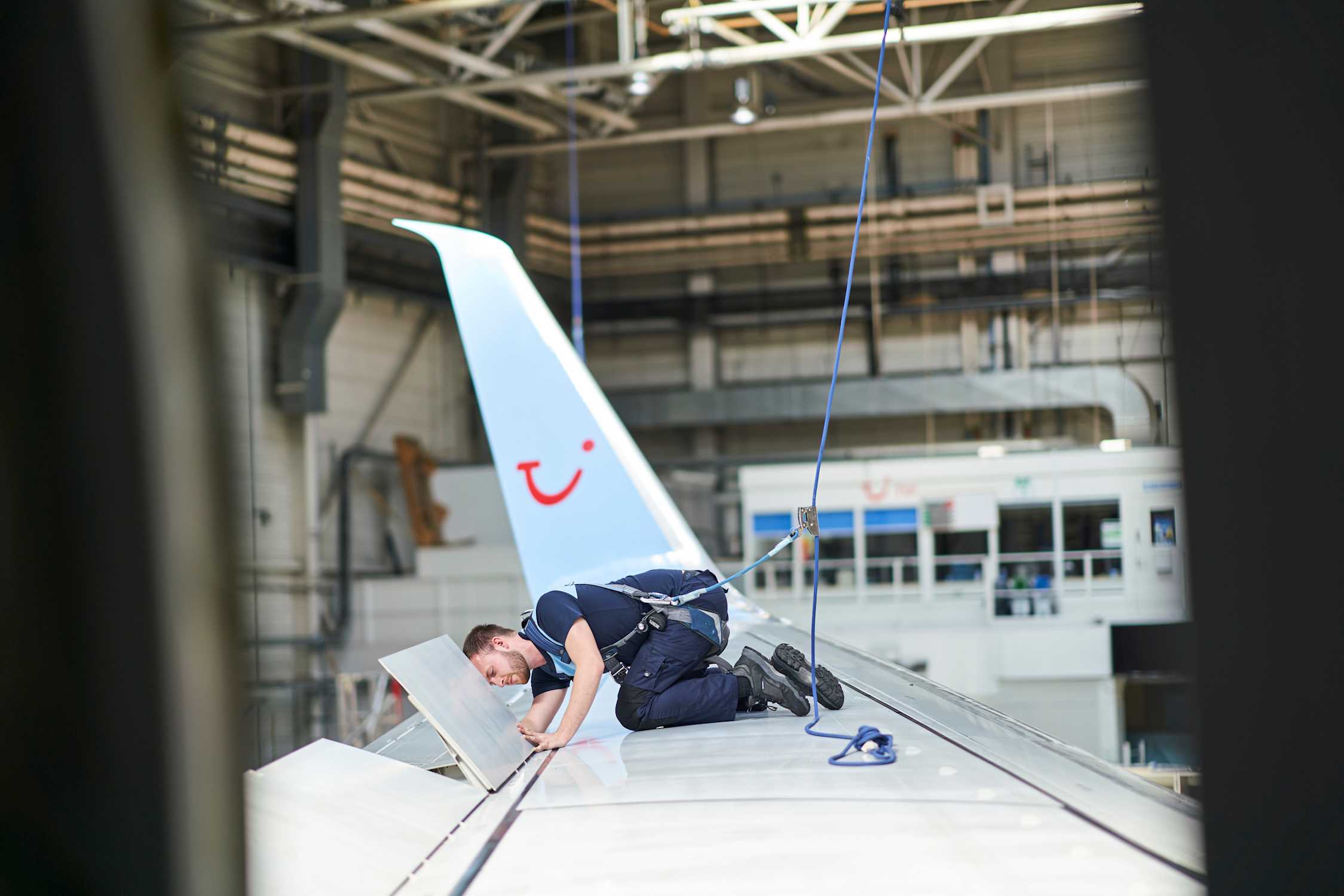 A man works on the flaps of an airplane wing in an aircraft hanger