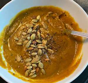 creamy pureed butternut soup garnished with raw pumpkin seeds