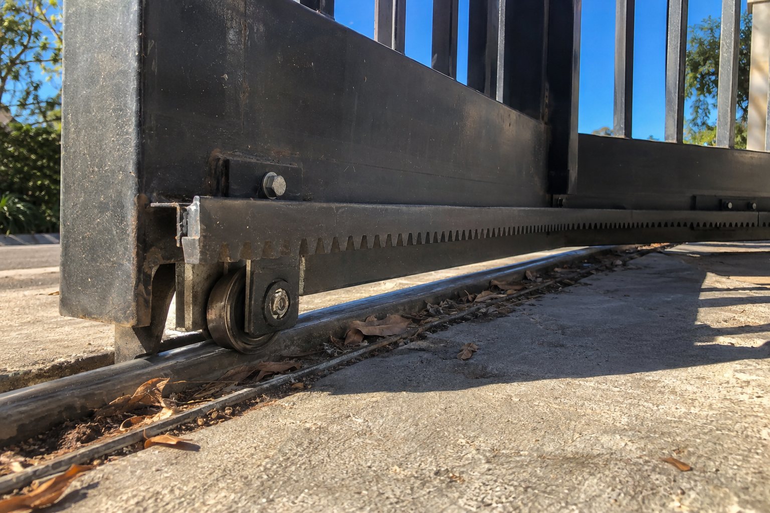 Base of a slide gate showing the drive rack, guide roller, and debris packed into the track