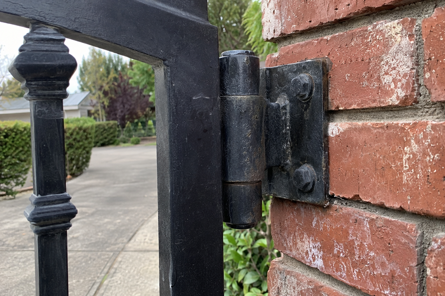Close-up of a heavy black steel gate hinge bolted to a brick masonry pillar
