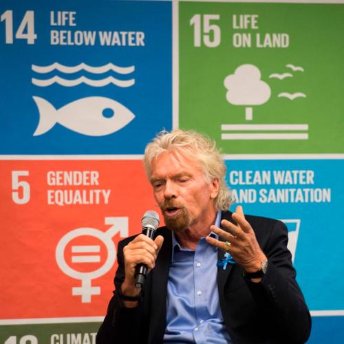 Richard Branson speaking into a microphone in front of a board talking about the UN Sustainable Development Goals