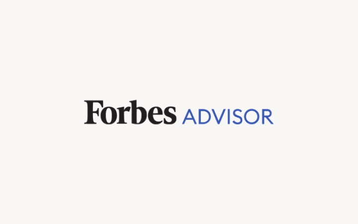 Forbes Advisor logo with black “Forbes” text and blue “ADVISOR” text on a light pink background.