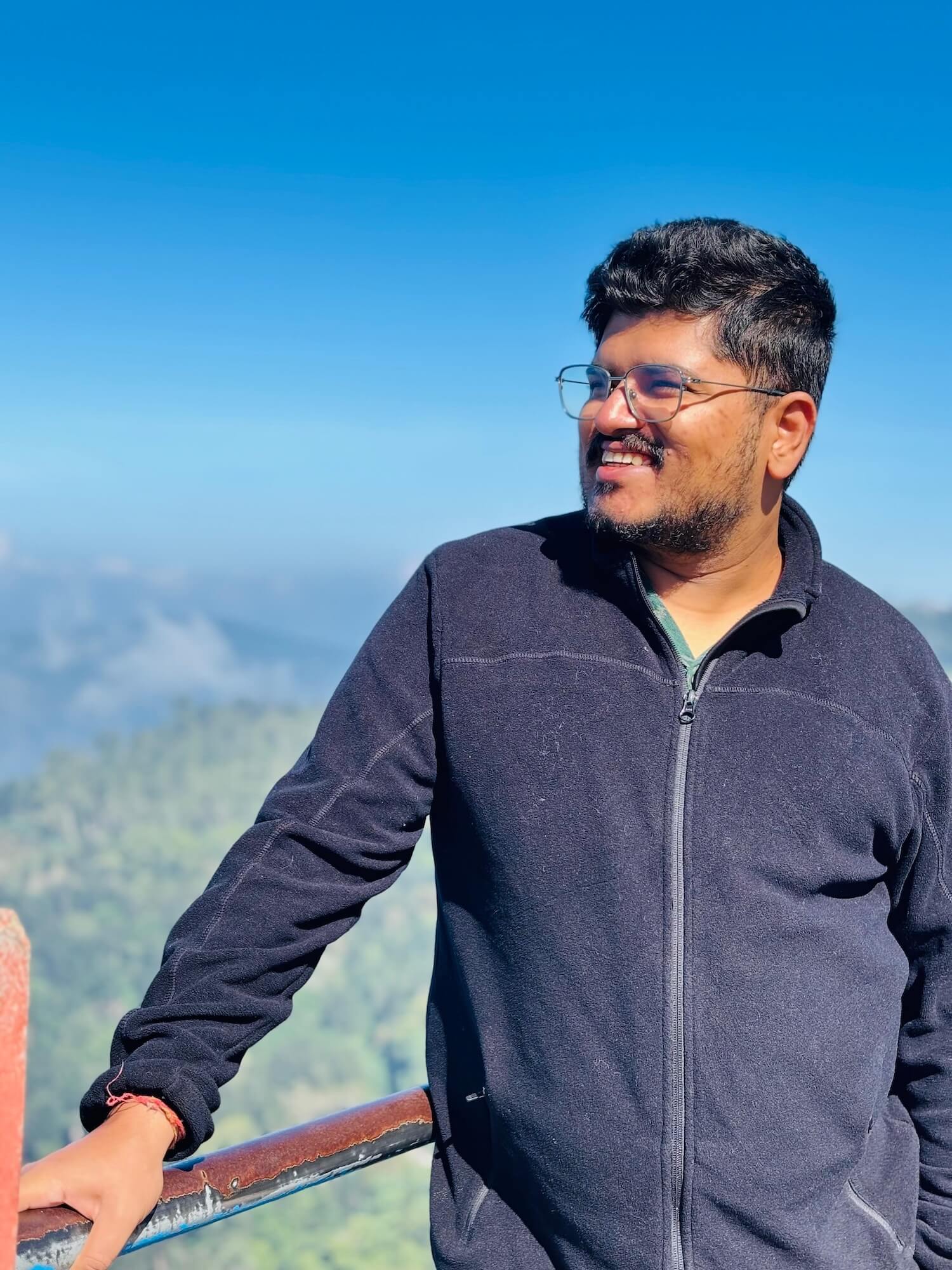 Rippler Nishant Arora standing at a viewpoint with trees and mountains in the distance. 