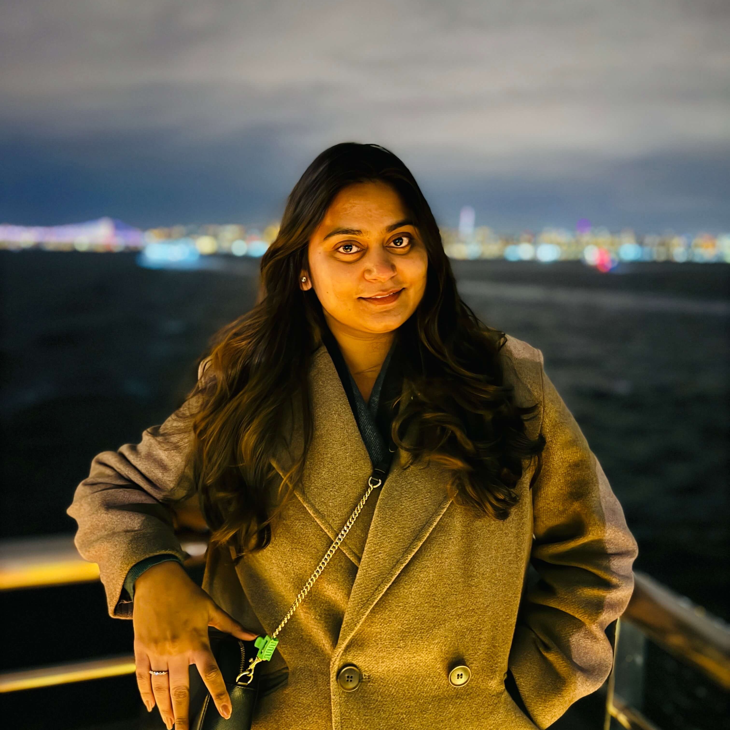 Rippler Apoorva Sharma at night with a lit up city on the horizon.