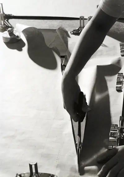 A paper patern is placed over the fabric and secured with clips and weights, then must be cut by hand with scissors