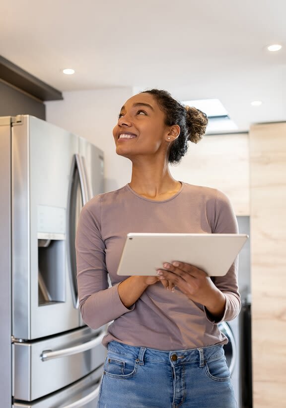 Woman in modern kitchen holding tablet, controlling Z-Wave smart lighting with secure encryption.