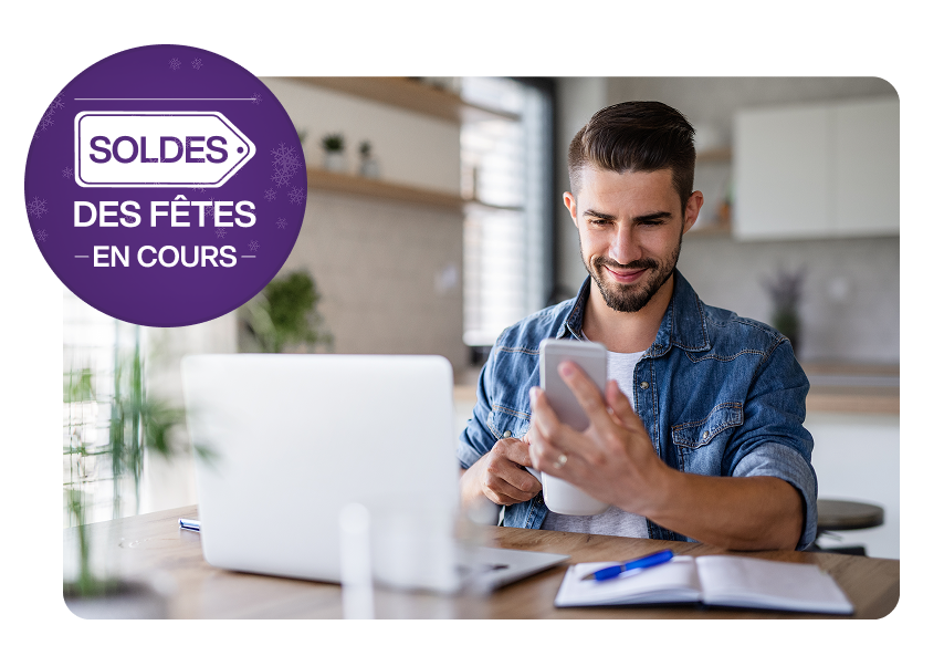 Un homme assis devant un ordinateur portable regarde son téléphone. Une cocarde sur la gauche indique « Soldes des Fêtes en cours ».
