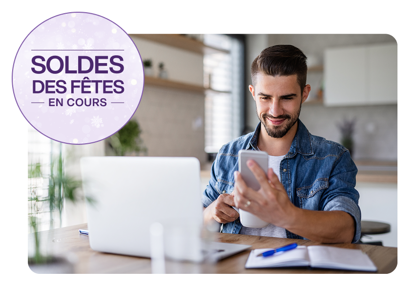 Un homme assis devant un ordinateur portable regarde son téléphone. Une cocarde sur la gauche indique « Soldes des Fêtes en cours ».
