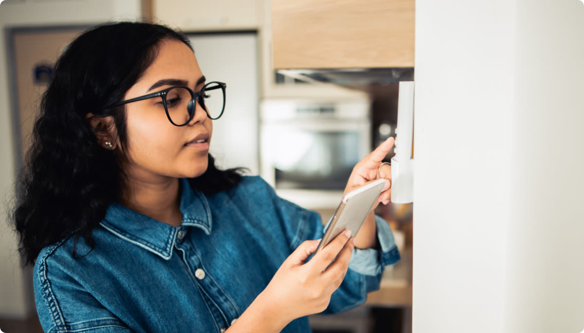 Une femme installe facilement un thermostat dans sa maison.

