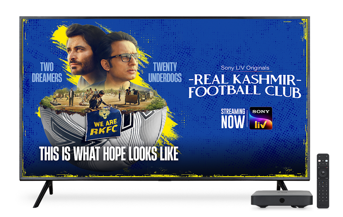 A TV, digital box and remote control. The TV screen displays the poster for Real Kashmir Football Club on Sony Liv.