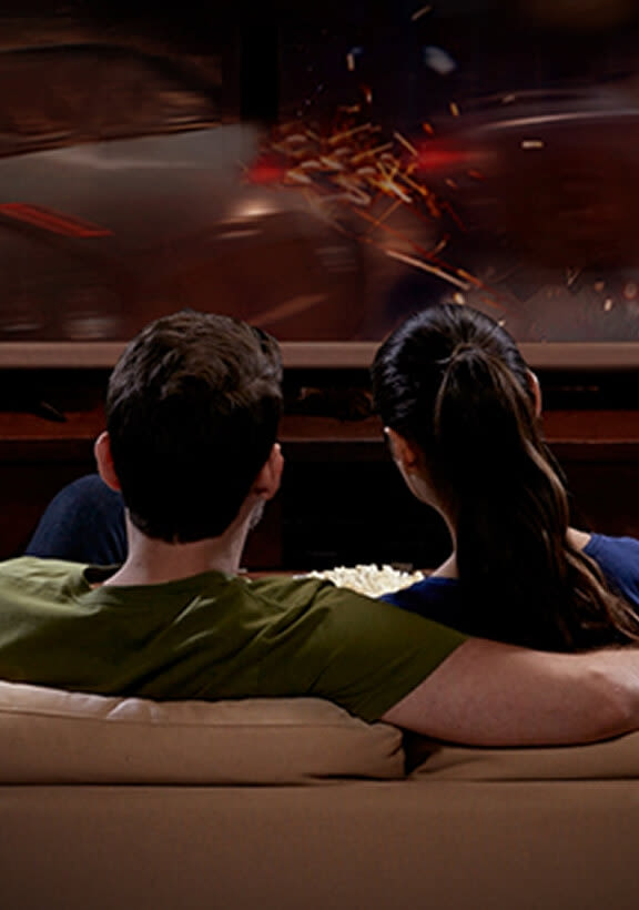 Couple relaxing on couch watching movie with ambient multicolour smart lighting creating cinematic atmosphere.