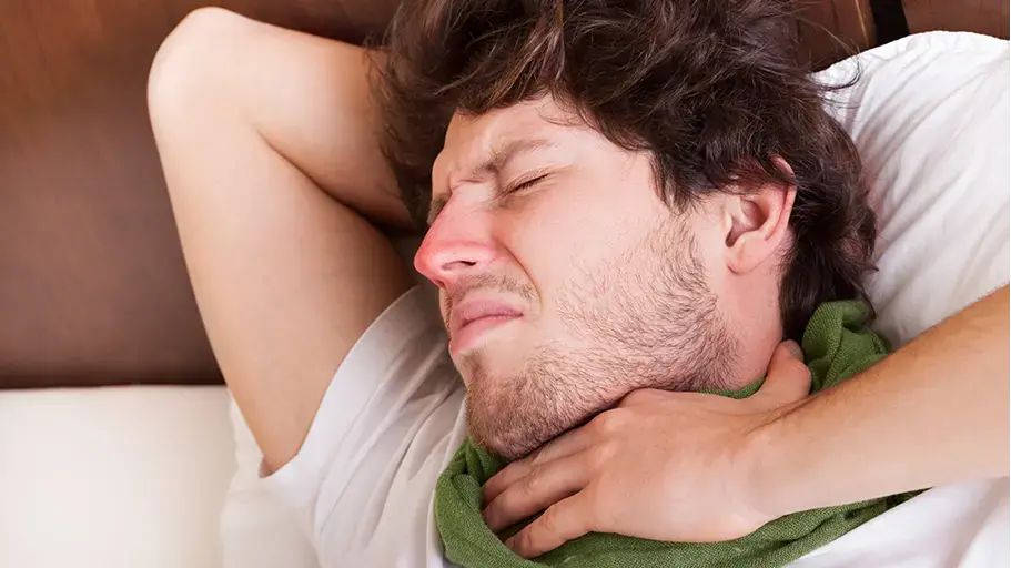 Person laying in bed experiencing a sore throat