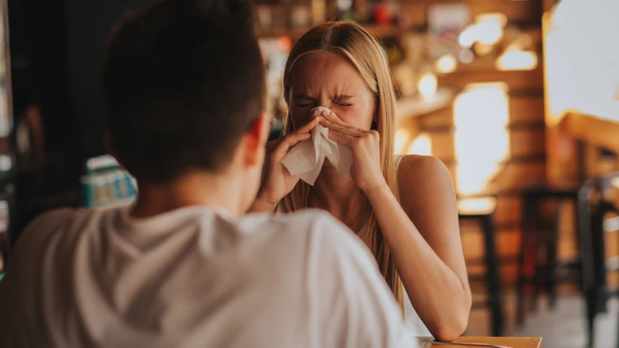 Woman sneezing in front of a man