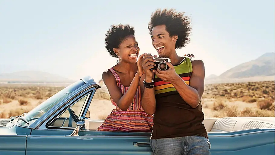 Two people outside in a covertible holding a camera