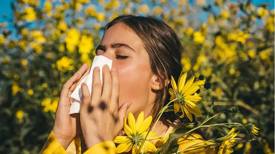  A woman blowing her nose outside surrounded by yellow flowers 