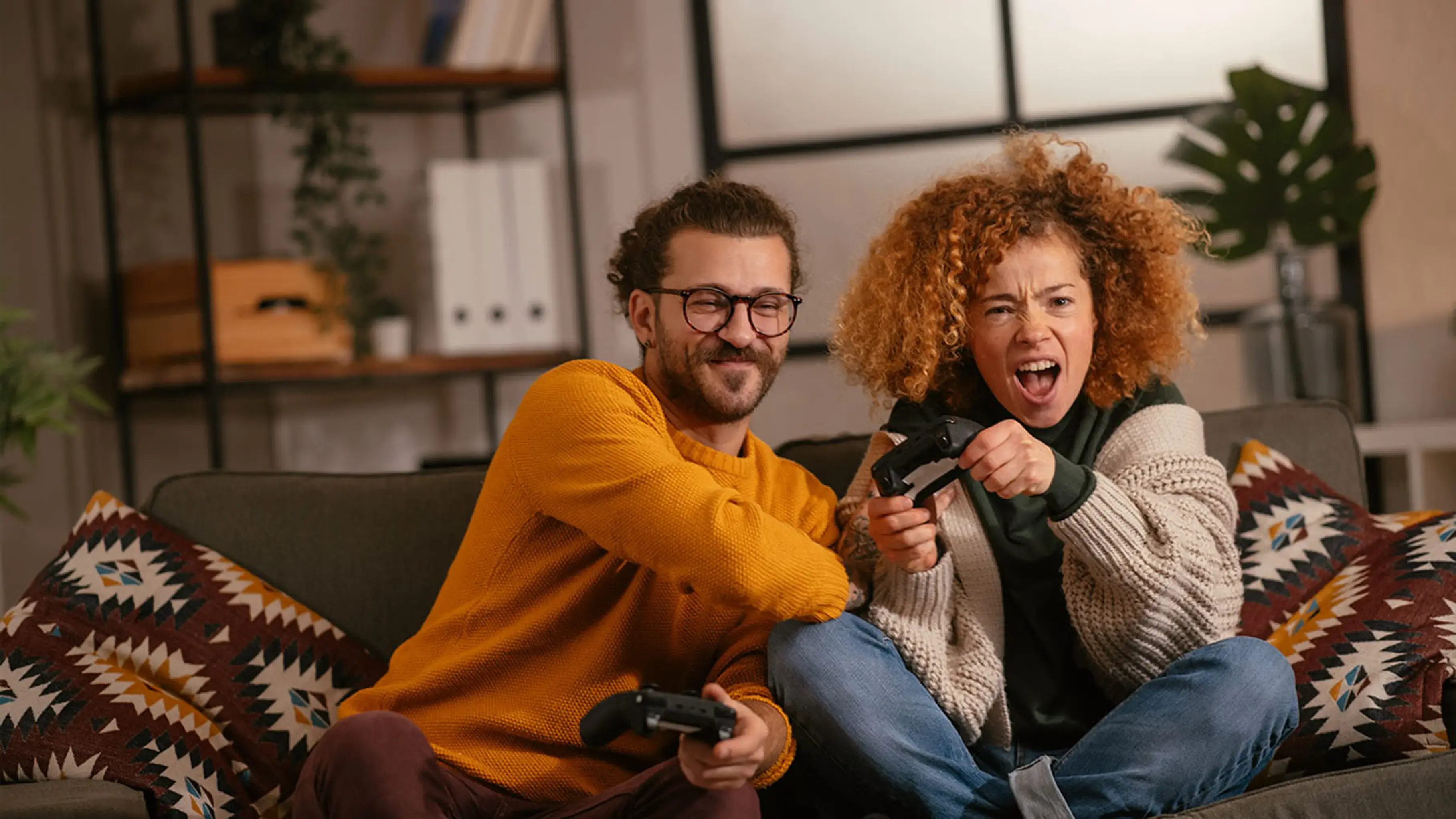 A man and a woman playing video games enthusiastically on the couch of a cozy living room