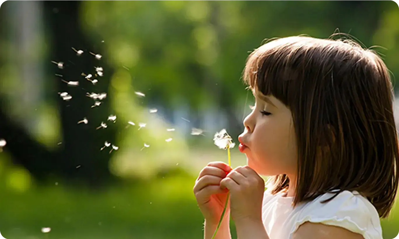 A child blowing on a dandelion, highlighting common triggers of kid's allergies during outdoor play.