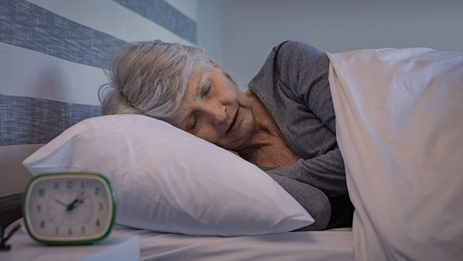 Mujer durmiendo sobre una almohada con un reloj en la mesa de noche