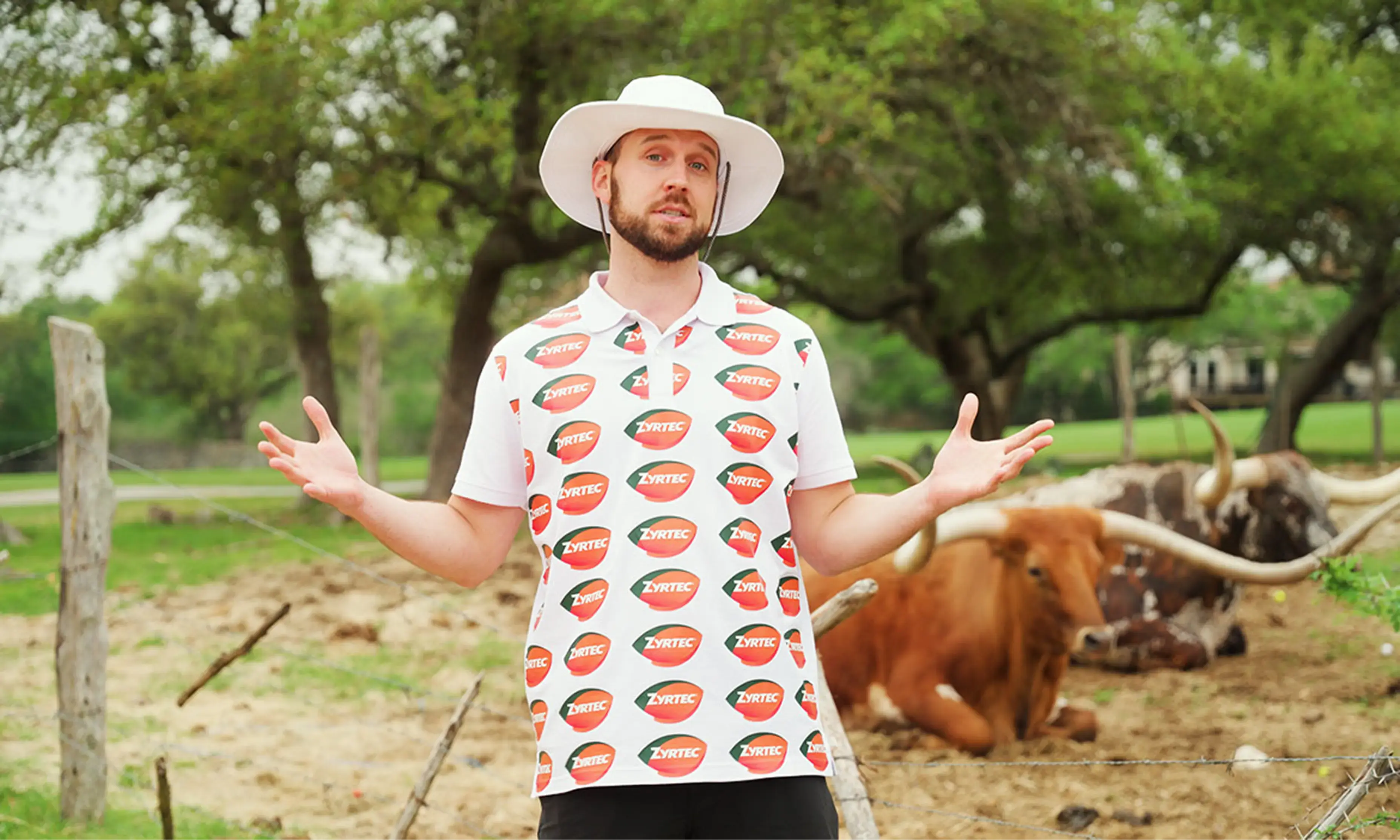 Trey Kennedy wearing a golf shirt bearing the ZYRTEC® logo and a hat, standing outdoors with a Texas Longhorn in the background and trees surrounding the area.