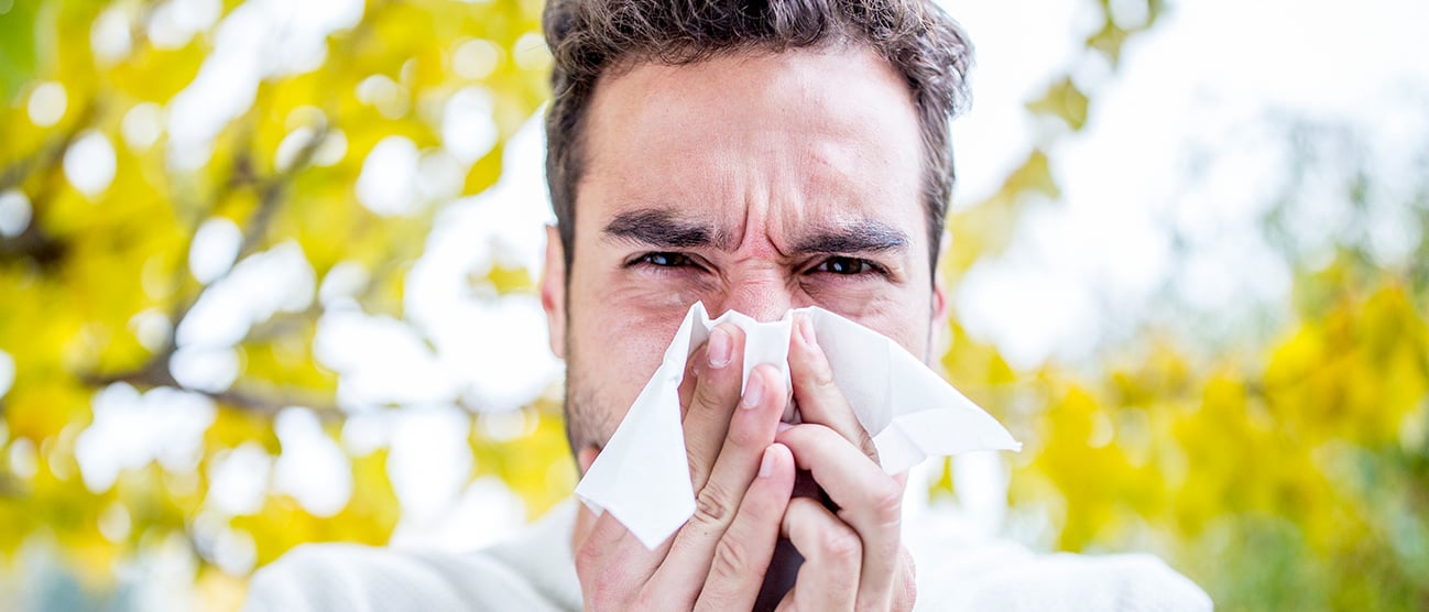 A man standing outside blowing his nose into a tissue