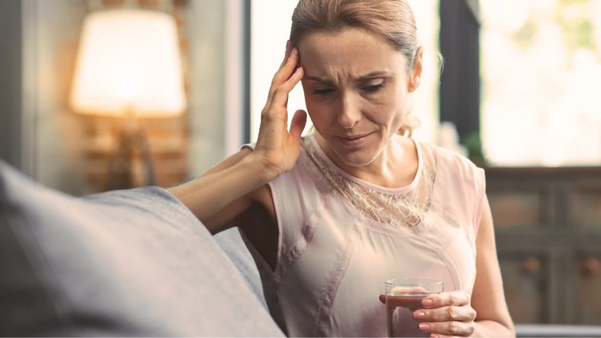 Mujer con dolor de cabeza sosteniendo un vaso de agua