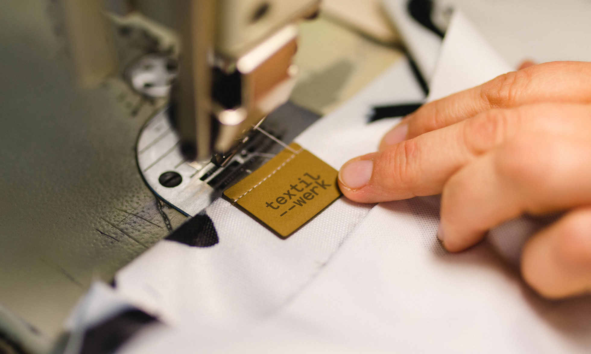 Eine textilwerk Lederetikette wird mit einer Nähmaschine angenäht