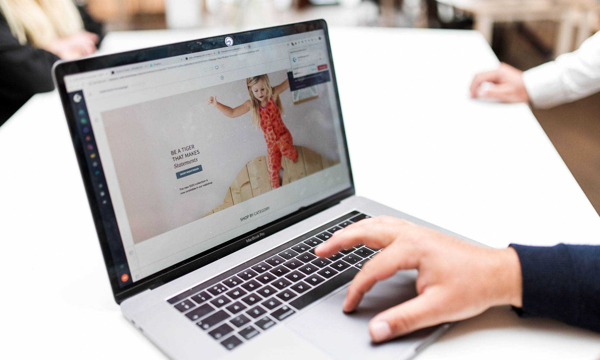 Eine Hand auf einem Trackpad eines Laptops zeigt eine Website für Kinderkleidung