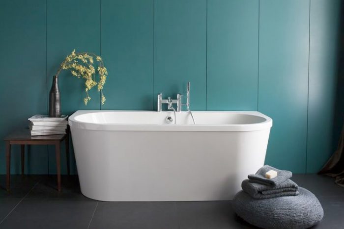 Modern minimalist white bathtub with a chrome faucet in front of a teal-coloured tiled wall