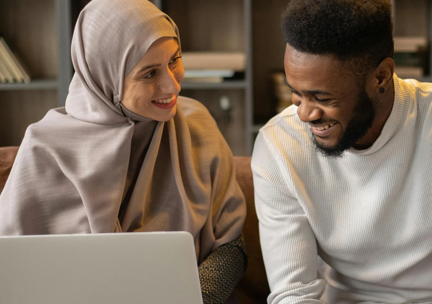 Two people with happy expressions, looking at laptop screen