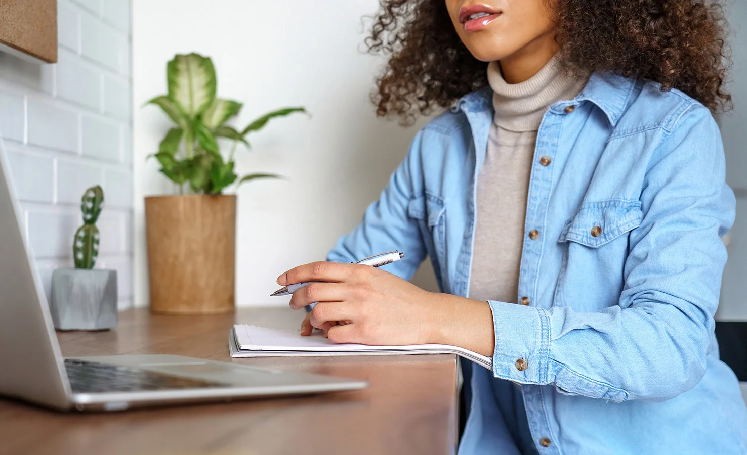 Woman sitting a at desk looking at a laptop and writing in a notebook