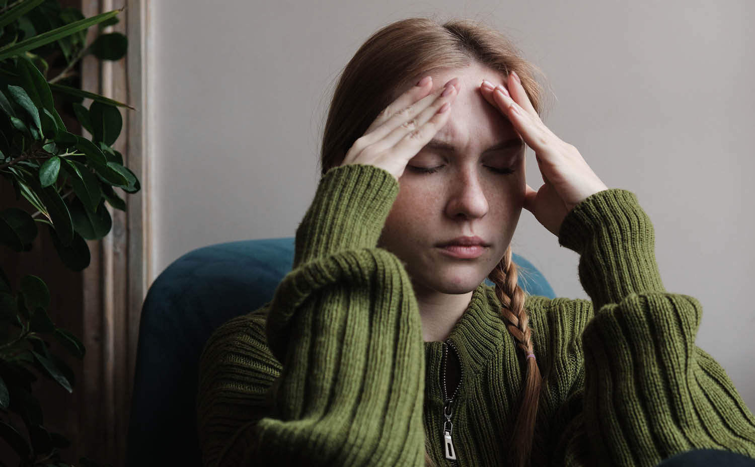 A woman holds her head in her hands and closes her eyes