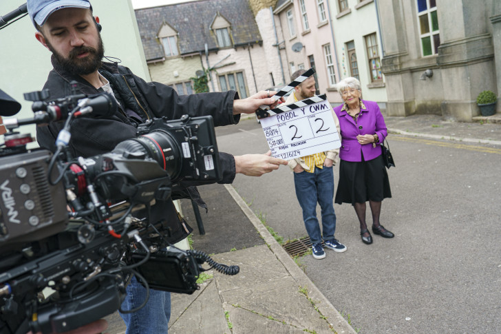 A photograph of actors and a camera operator with clapper board - Pobol y Cwm on the clapper.