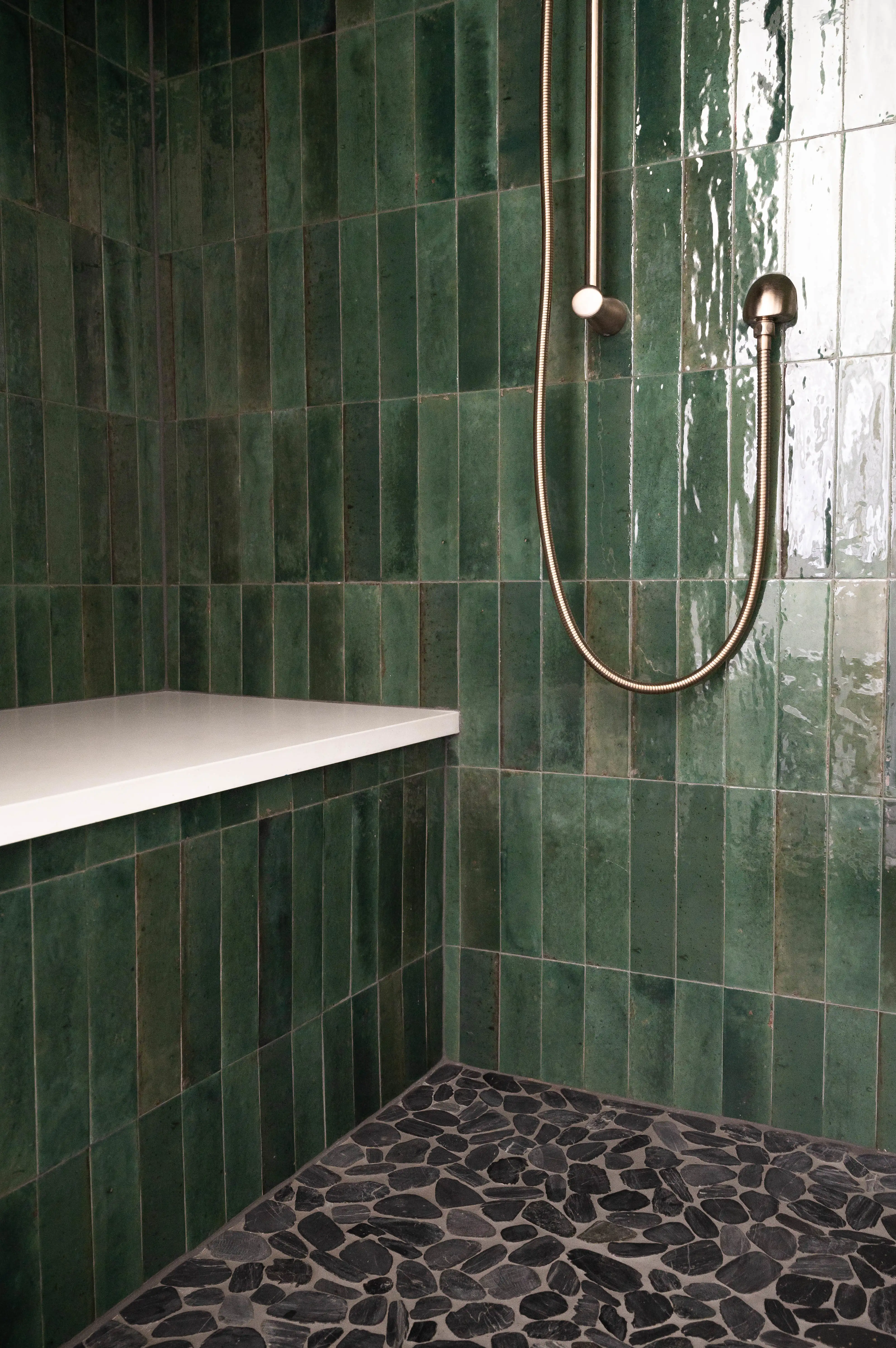 A rich green tile shower with brass hardware and a black natural stone mosaic floor.