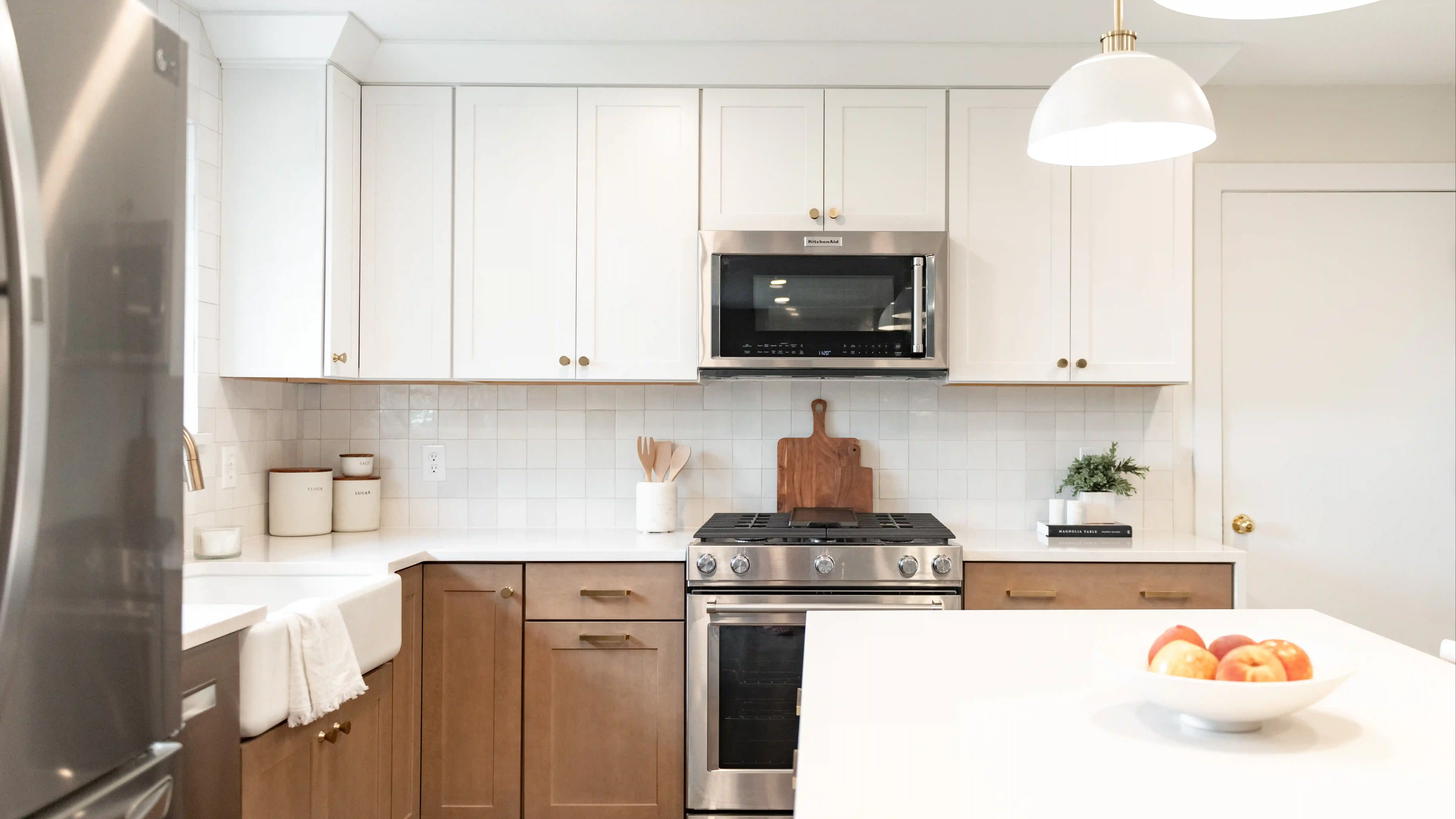 A kitchen with natural wood colored cabinetry, a white tile backsplash, and white quartz countertops. 