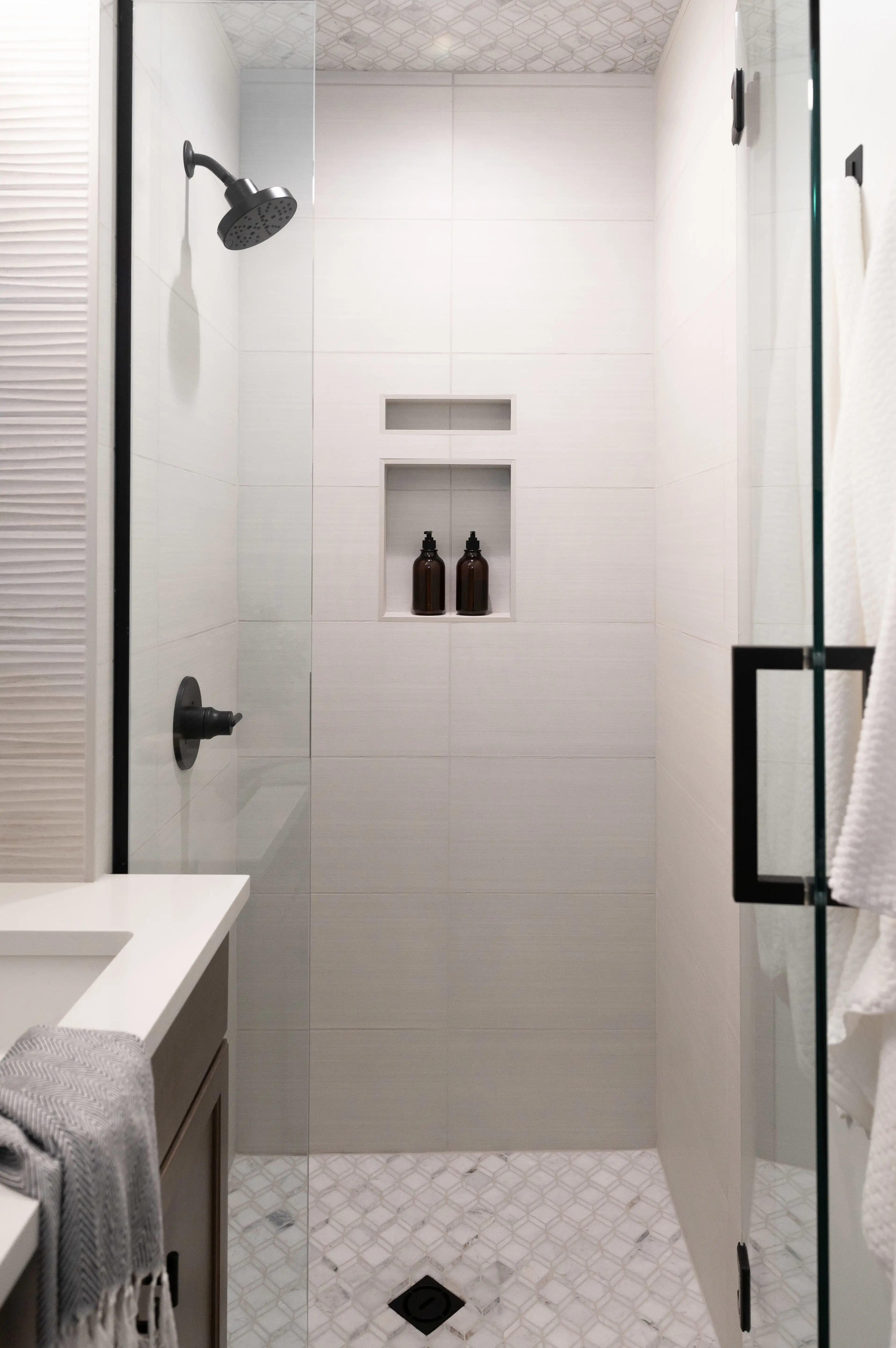 A cream colored, wavy textured tile shower with bronze hardware and a clear glass door. 
