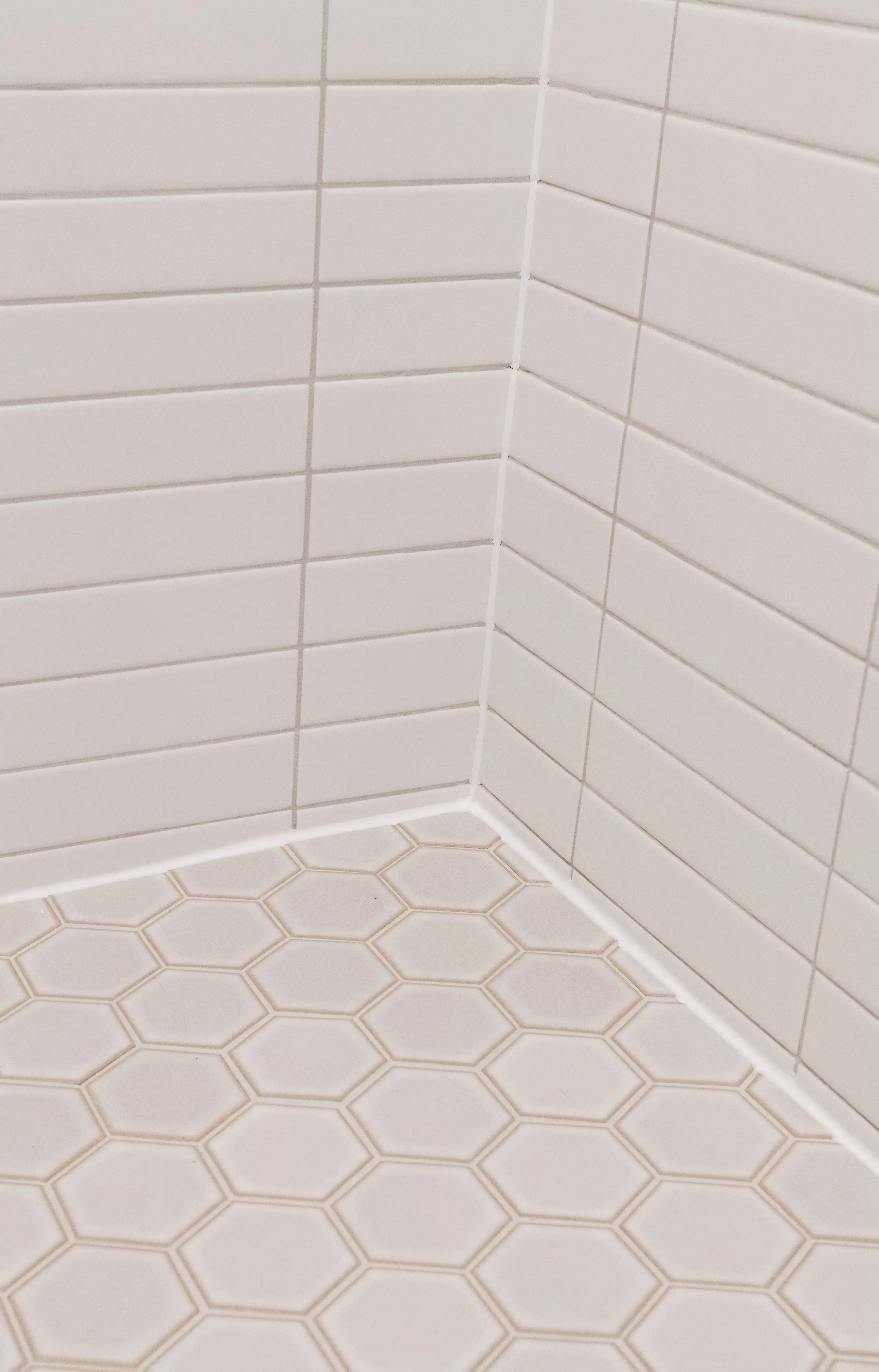 A white subway tile shower with cream hexagon tile floor. 