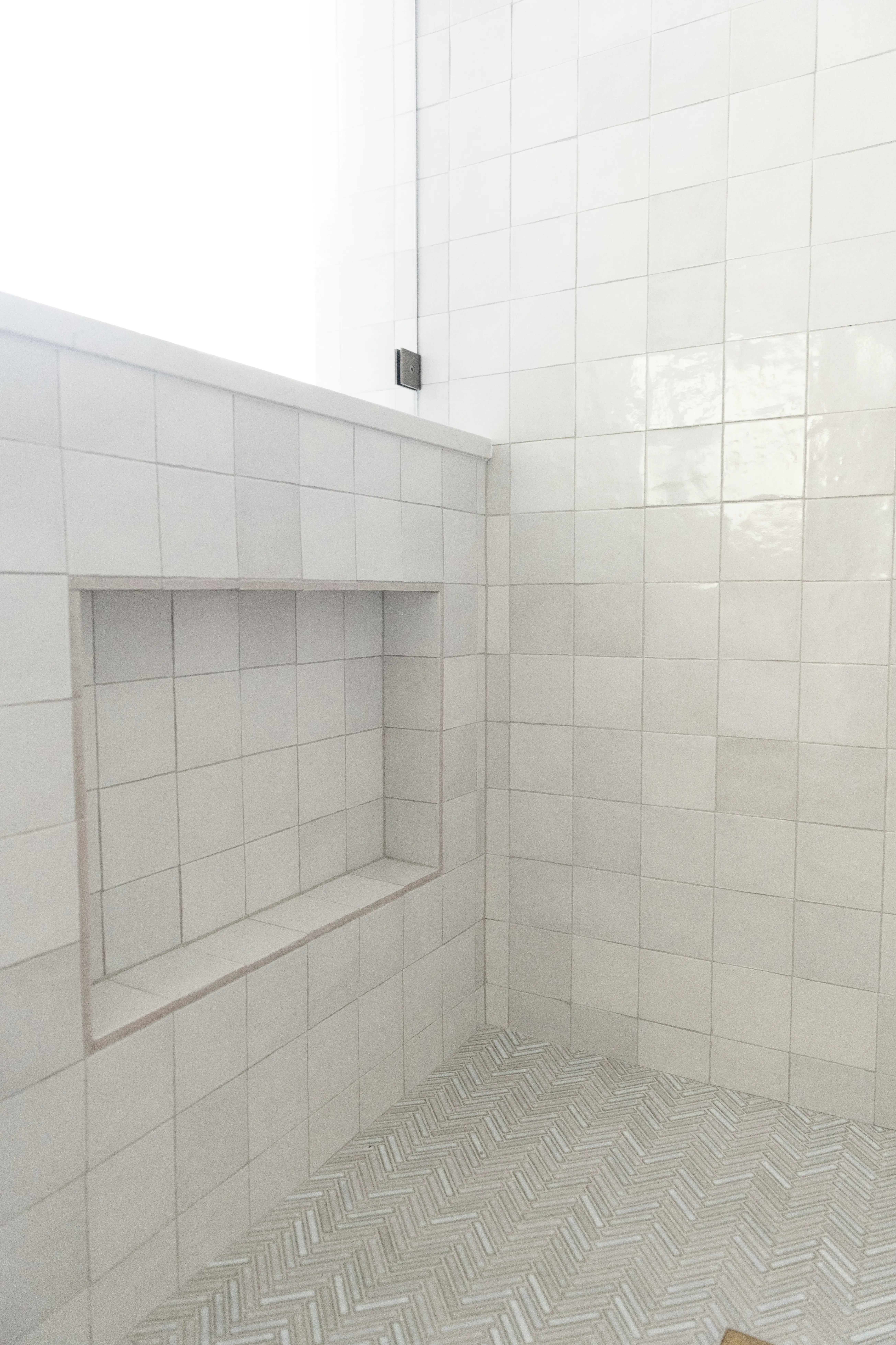 A shower with multi toned ivory square tiles on the shower surround and chevron patterned floor tiles. 