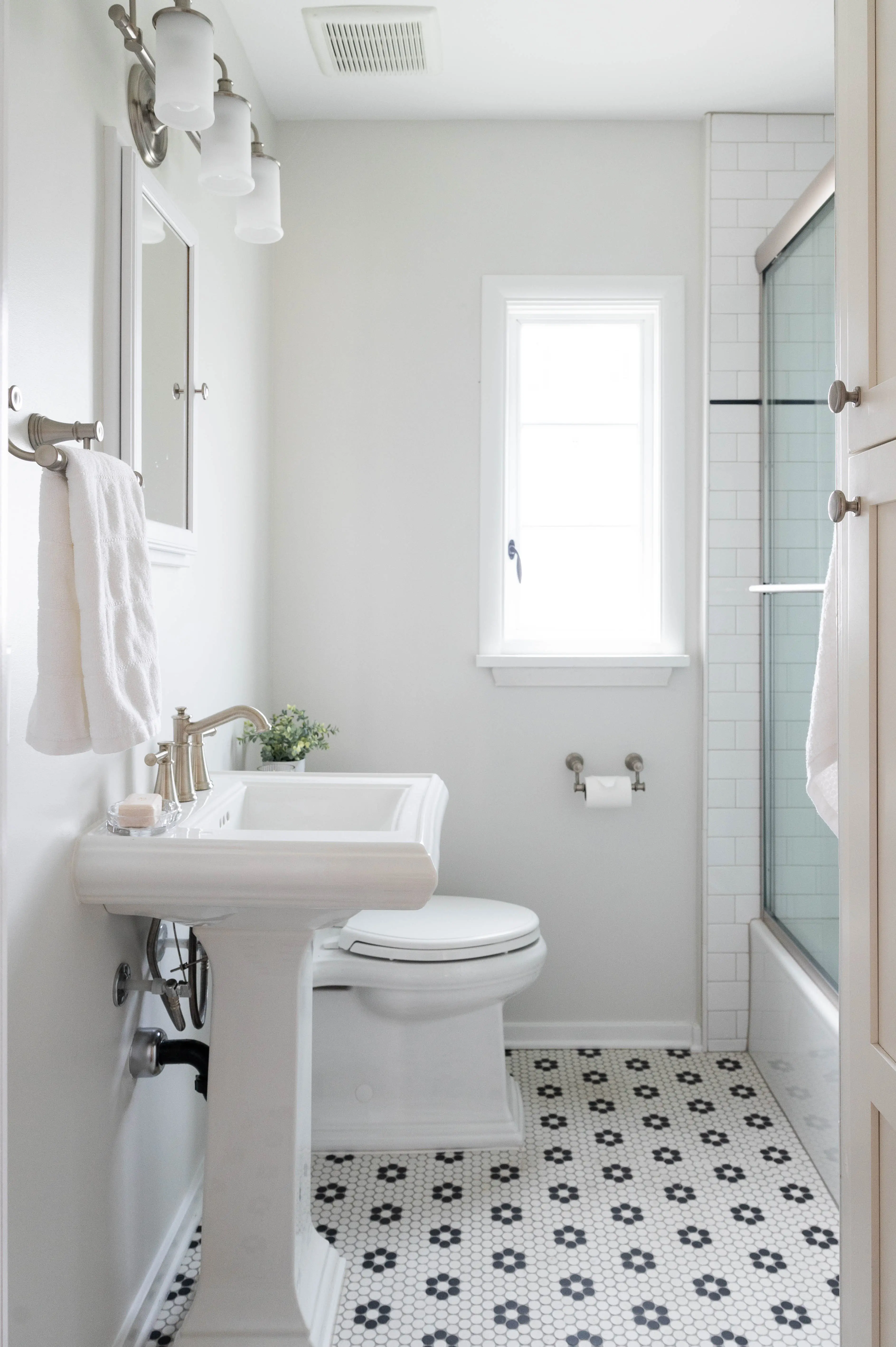 A small bathroom with a pedistal sink, black and white hex pennytile flooring, and all white accents. 