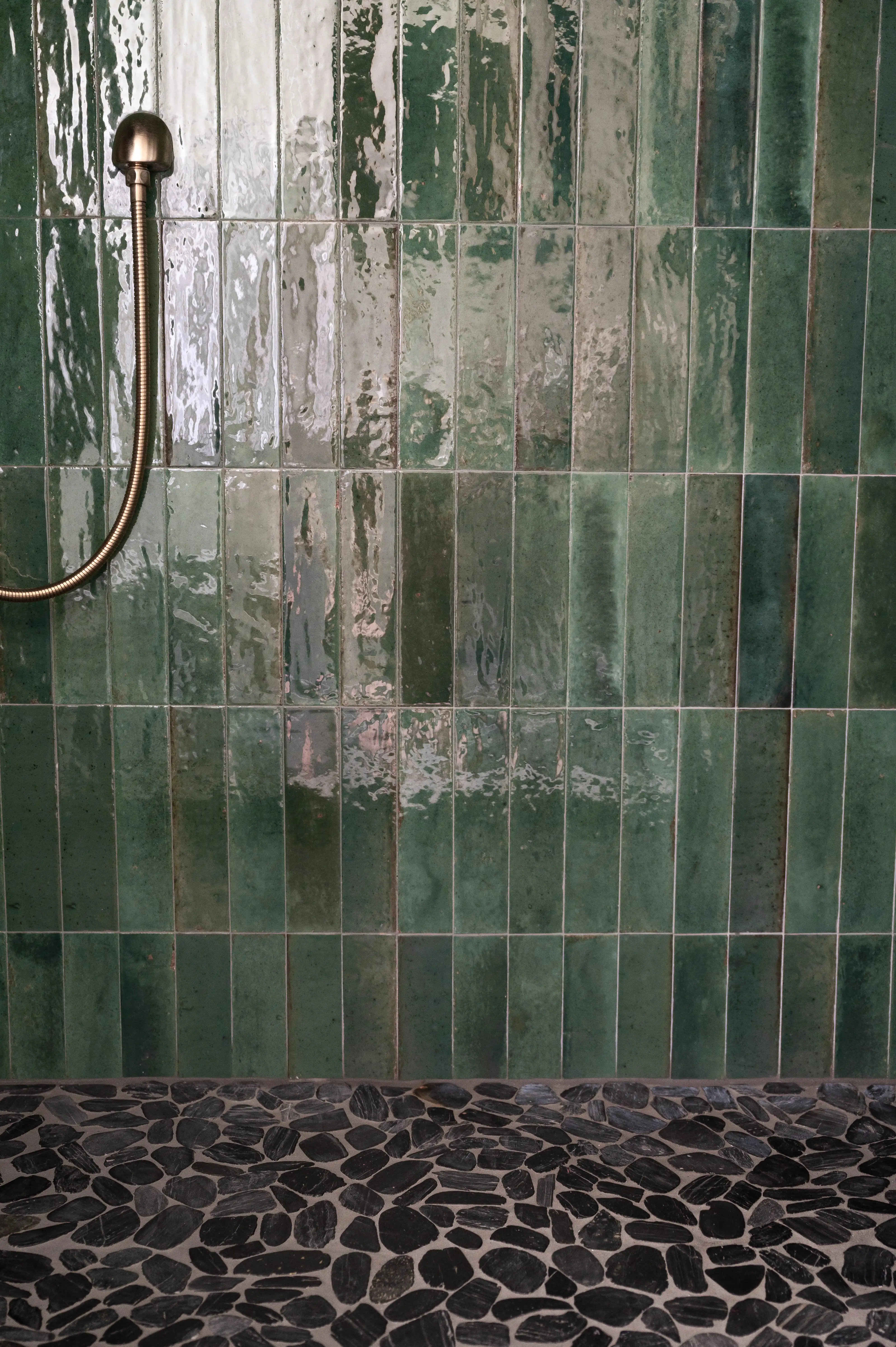 Rich green shower tiles are shown. On the shower pan is a black natural stone mosaic. 