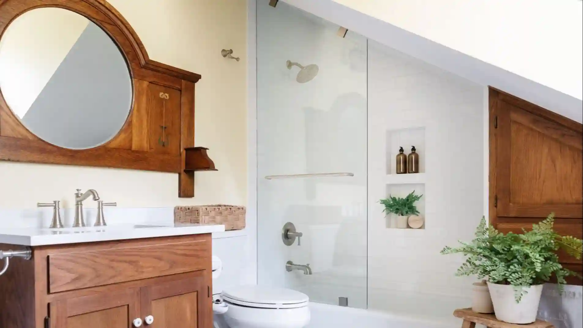 A bathroom with and angled ceiling above the shower. Cherry wood is used throughout the bathroom in the vanity, wall, and built in wood framed circular mirror, all matching. 