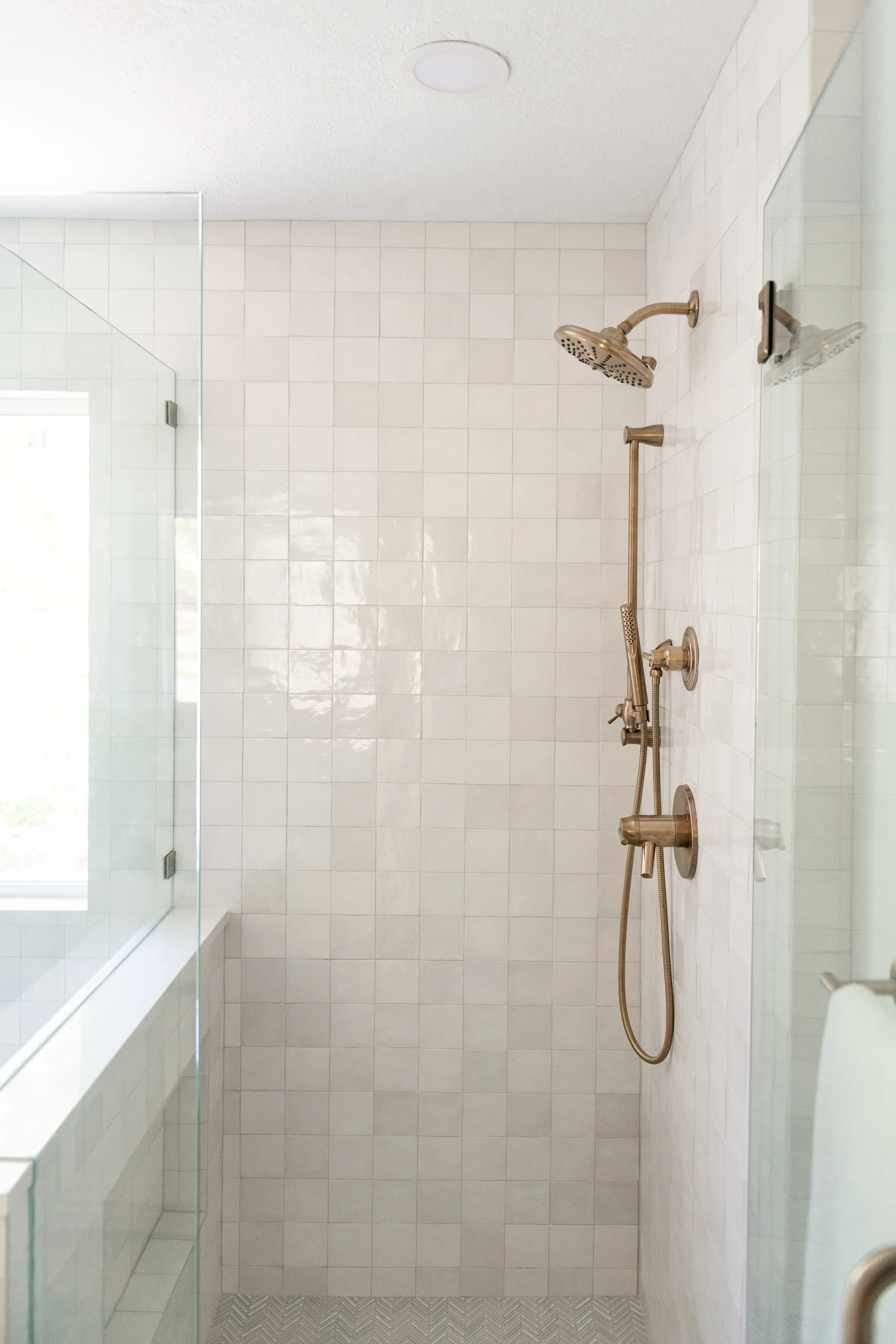 A white tile shower with brass hardware. 