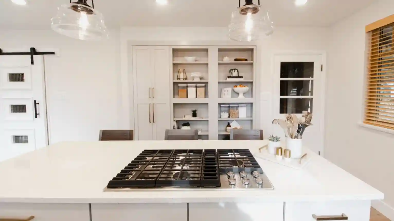 An all white kitchen with built in shelving and cabinets on the backwall. 