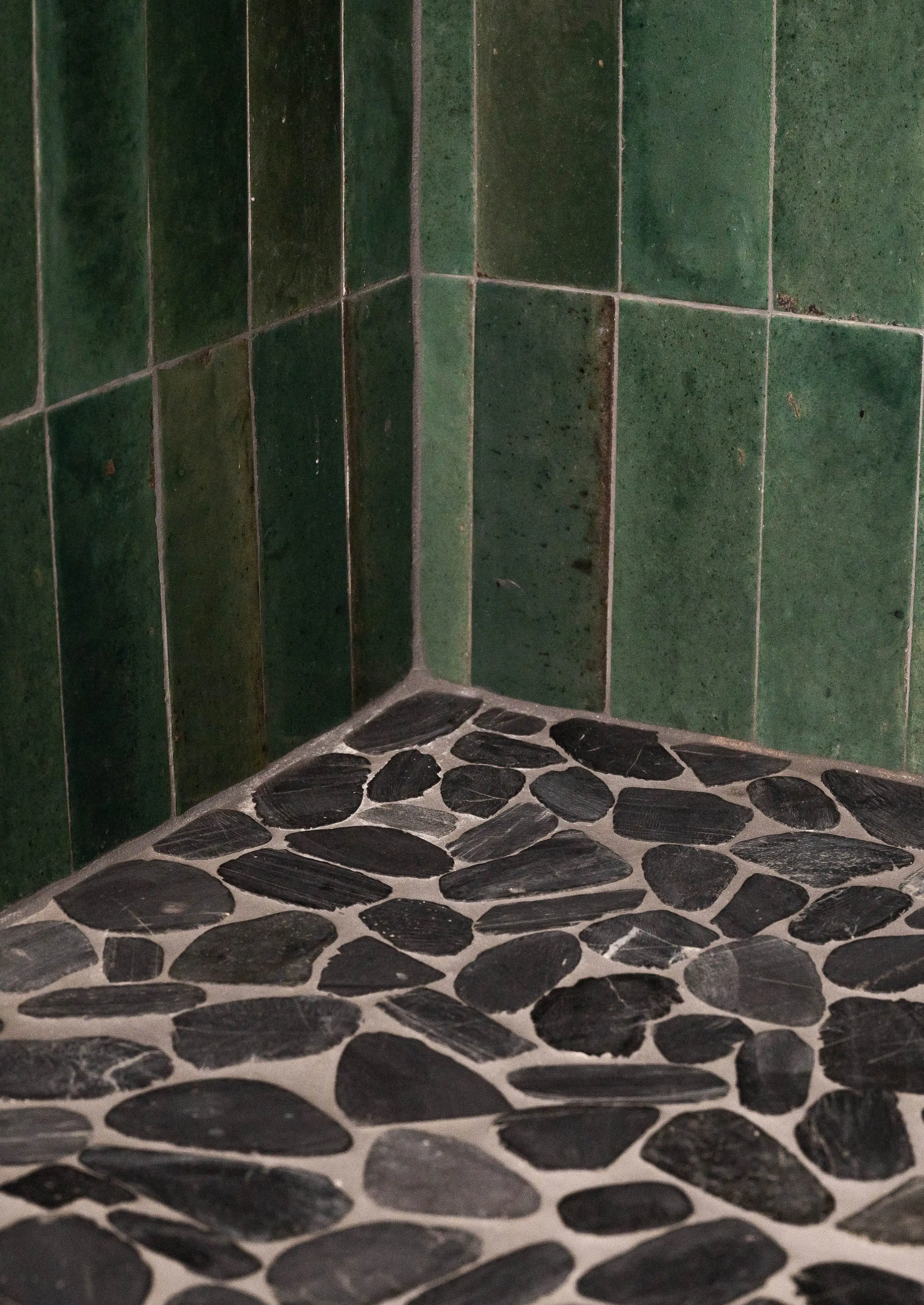 Rich green tile shower surround with black, natural stone mosaic flooring. 